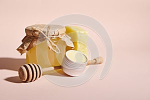 Still life. Organic honey and wooden stick on pink backdrop, next to natural handmade cold-pressed soap and can of wax