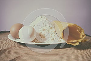 Still life photo, colored eggs, white plate with flour and homemade pasta, on pine wood