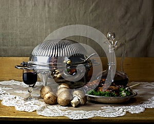 Still life photo of decanter and glass of port, antique chafing dish, mushrooms and roasted chicken