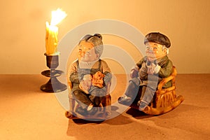 Still life photography with lovely senior couple doll siting rocking bamboo chair with light of the candle in the dark on wood