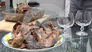 Still life, pieces of roast duck in a plate in the foreground on a glass table, near glass glasses. In the background, a