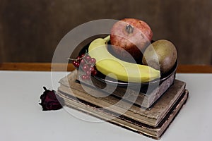 a still life with a pile of old books, fruit on a plate