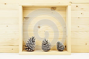 Still life of pine cones with snow in wooden square box.