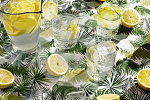 Still life with a pitcher of lemonade crystal glasses with ice and lemon, tablecloth with green flowers. Refreshing summer drink