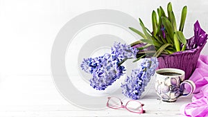 A still life of purple Hyacinth flower blooms with a cup of coffee in front.