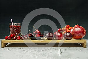 Still life of red berries with a glass of juice with a straw on a bamboo wooden board with cherries