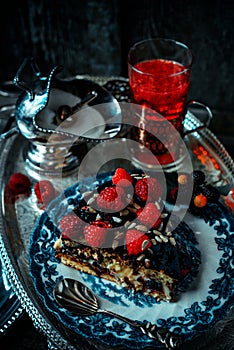 Still life in royal style. Close up piece of chocolate cake with raspberries on old blue plate, beside glass fruit drink on silver