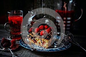 Still life in royal style. Close up piece of chocolate cake with raspberries on old blue plate, beside glass fruit drink on silver