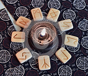 Still life with runes around burning black candle on tarot cards