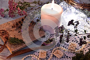 Still life with runes, healing herbs, witch diary, white candle and shining bottle on lace.