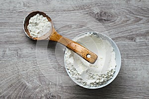 Still life of rural cuisine. White flour in a porcelain bowl with a wooden spoon handmade on a wooden background