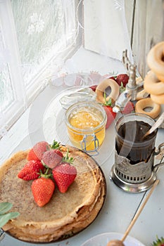 Still life in the Russian tradition for Maslenitsa pancakes with honey and strawberries,tea in faceted glass with bagels