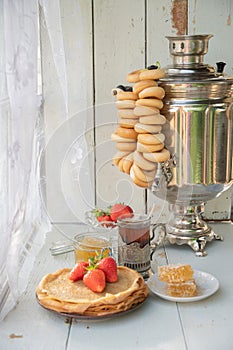 Still life in the Russian tradition for Maslenitsa, pancakes with honey and strawberries, tea from a samovar with bagels