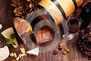 Still life in a rustic style. Grapes on a wooden table with a bottle of wine and meat and cheese. Antipasto and red wine