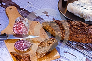 Still life salami cut on wooden table with bread with cereals and fresh cheese