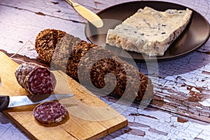 Still life salami cut on wooden table with bread with cereals and fresh cheese