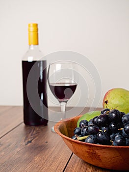 Still life scene. Bottle of red wine and one glass and wooden bowl with dark grapes. Bright color background. Food industry