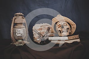 Still life with the skulls in books, old lamps and guns crossed