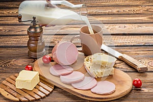 Still life of Sliced boiled sausage with ingredients. rural breakfast - boiled sausage, bread, milk, butter, tomatoes over wooden
