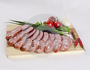 Still life with sliced smoked sausage greens and tomatoes on a white background