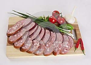 Still life with sliced smoked sausage greens and tomatoes on a white background