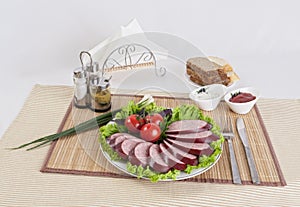Still life with sliced smoked sausage greens and tomatoes on a white background