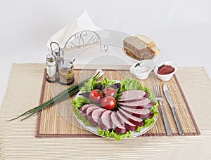 Still life with sliced smoked sausage greens and tomatoes on a white background