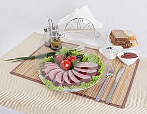 Still life with sliced smoked sausage greens and tomatoes on a white background