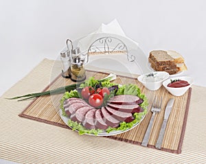 Still life with sliced smoked sausage greens and tomatoes on a white background