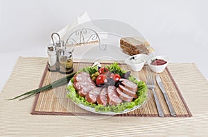 Still life with sliced smoked sausage greens and tomatoes on a white background