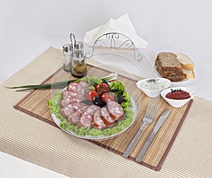 Still life with sliced smoked sausage greens and tomatoes on a white background