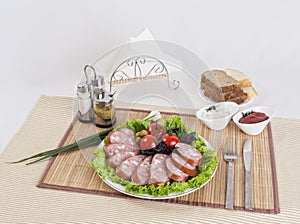 Still life with sliced smoked sausage greens and tomatoes on a white background