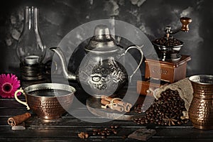 Still life in the style of an old photograph with a coffee grinder, coffee beans with an old lamp and a kettle with a