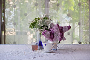 Still-life with tea, wine and a lilac bouquet