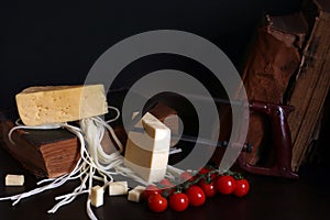 Still life with three cheeses  cherry tomatoes  old books and arm saw