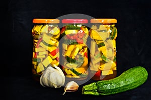 A still life of three glasses of pickled zucchini with some acsessoires arround and a black background