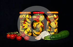 A still life of three glasses of pickled zucchini with some acsessoires arround and a black background