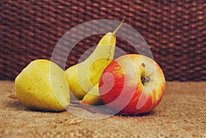 Still-life with three pears and one red apple on a brown background.