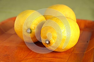 Still life with three ripe yellow lemons on brown tray