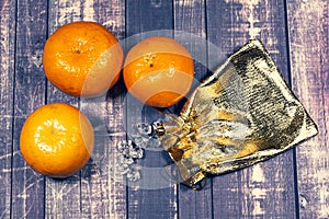 Still-life. three tangerines, a small pouch and glass stones on a dark wood background