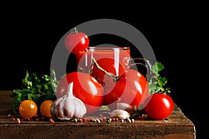 Still life with tomatoes, parsley, garlic and tomato juice on wooden boards. On a black background.