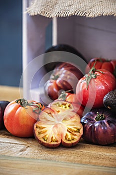 Still life of tomatoes of various types with some chopped, a pink wooden box on a wooden board