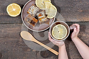 Still life top view. Children`s hands hold a mug with warm tea with lemon and honey in a plate