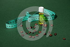 Still life transparent bottle of massage anti-cellulite oil, measure tape and coffee beans scattered on green background