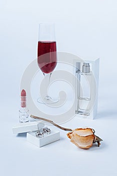 A still life with a transparent perfume bottle, a faded rose, a lipstick, a box with the silver earrings, and the glass