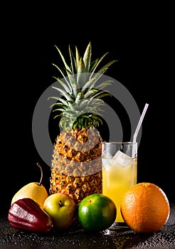 Still life with tropical fruits and glass of juice on a black r