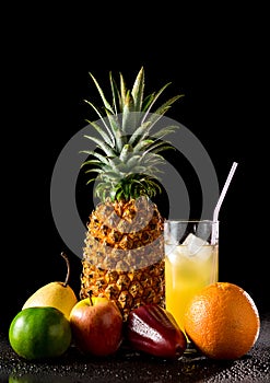 Still life with tropical fruits and glass of juice on a black r