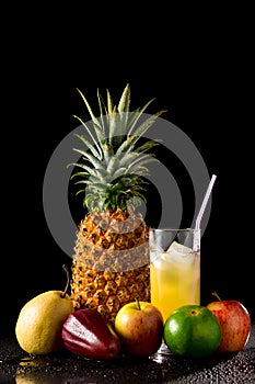 Still life with tropical fruits and glass of juice on a black r