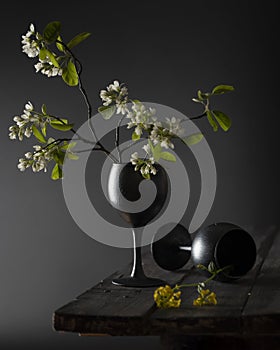 Still life with two black glasses and flowers on wooden table.