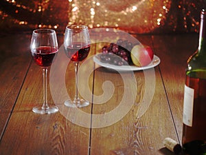 Still life with two glasses of red wine in focus, Bottle and cork in foreground out of focus, Plate with grapes and apple out of